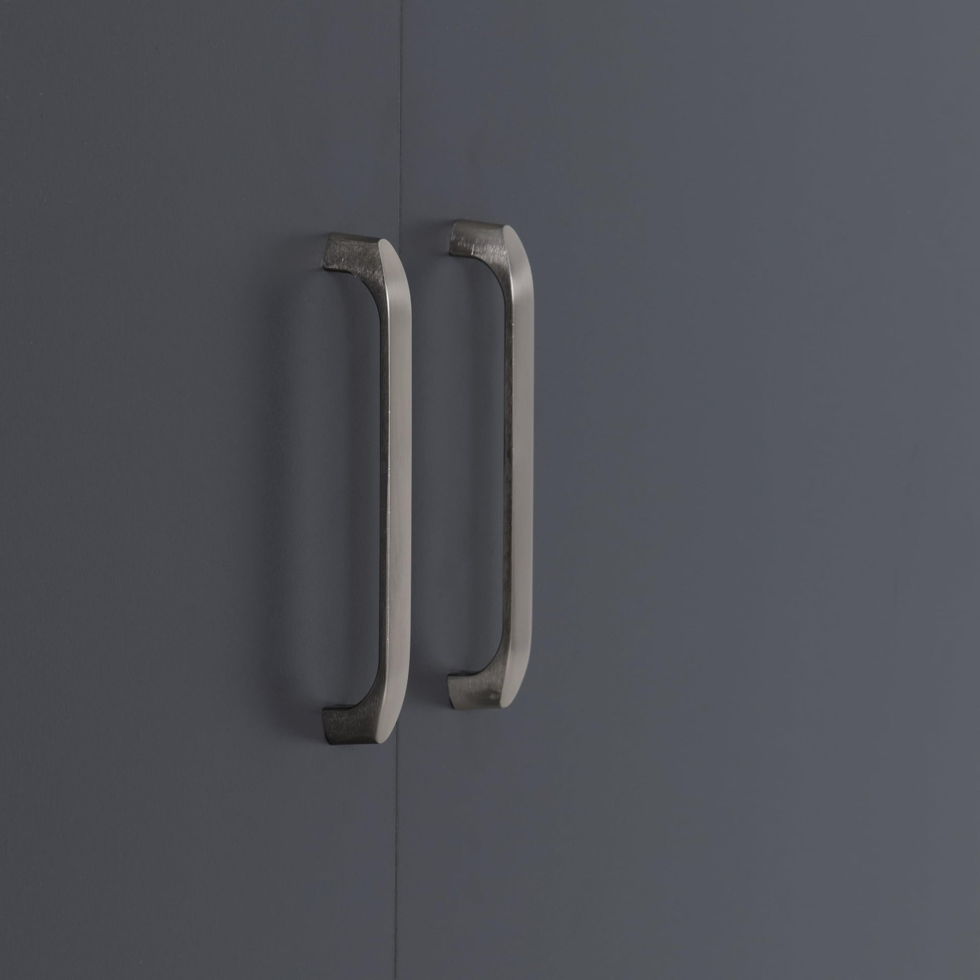 Close-up of two brushed metal vertical handles mounted on dark grey wardrobe doors