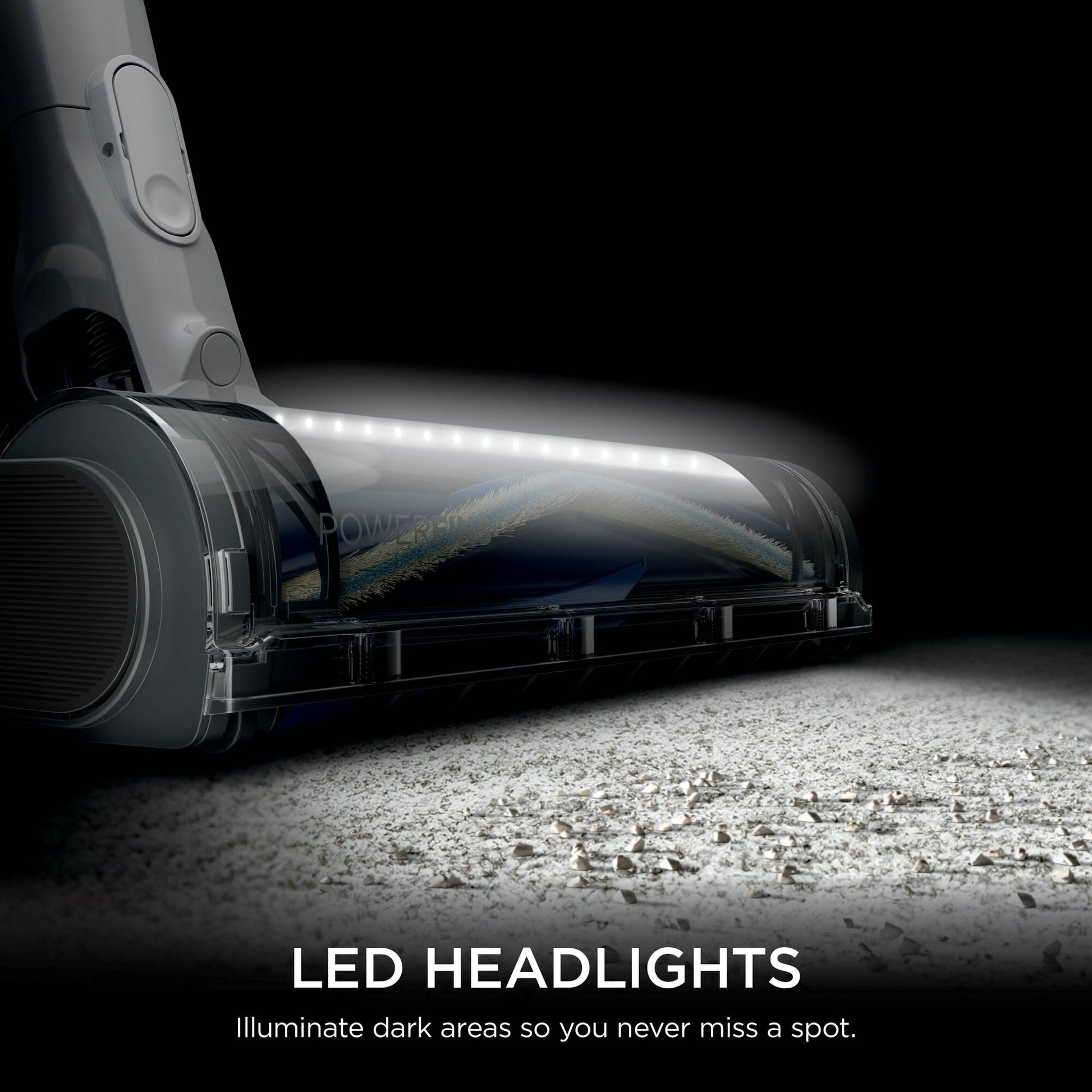 Low-angle close-up of the vacuum brushroll with LED headlights casting light across the floor.