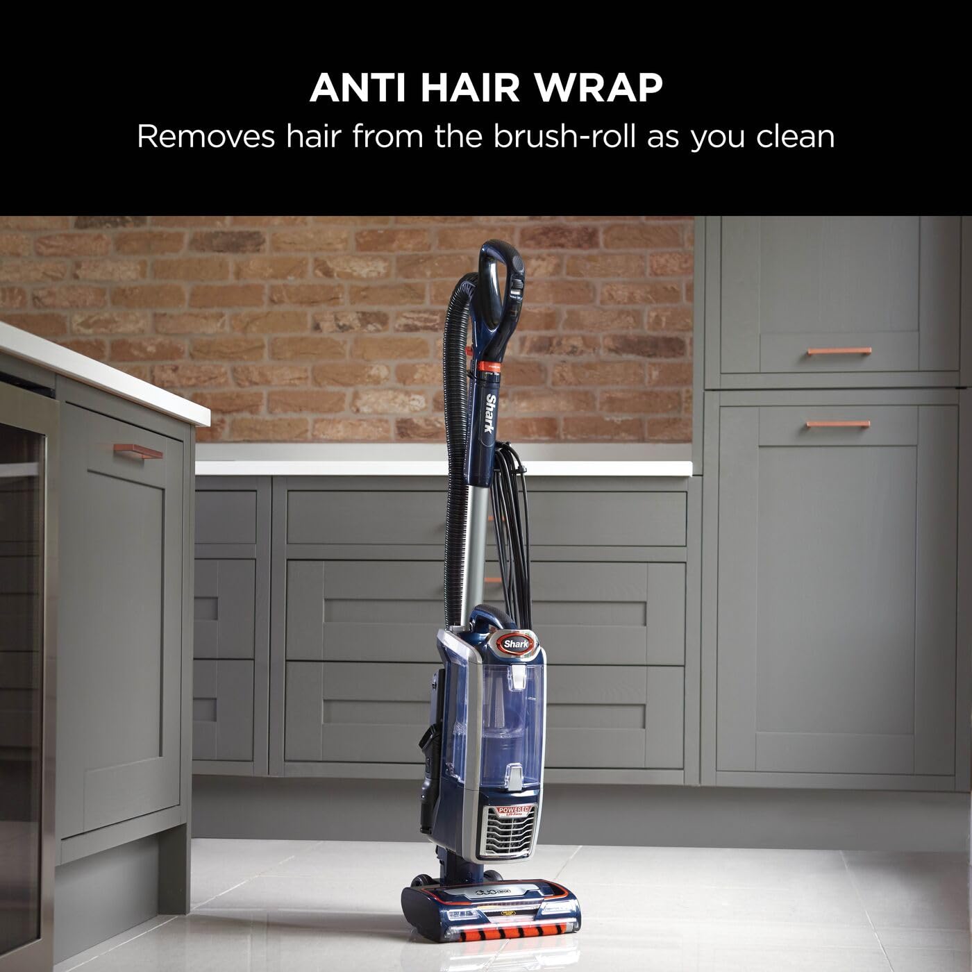 Shark upright vacuum standing in a modern kitchen with grey cabinets and a brick backsplash, 'Anti Hair Wrap' header visib…