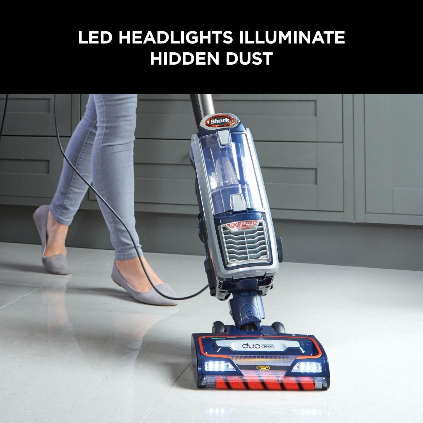 Close-up of the DuoClean floorhead with LED headlights and the upright vacuum's clear dust cup on a tiled floor.