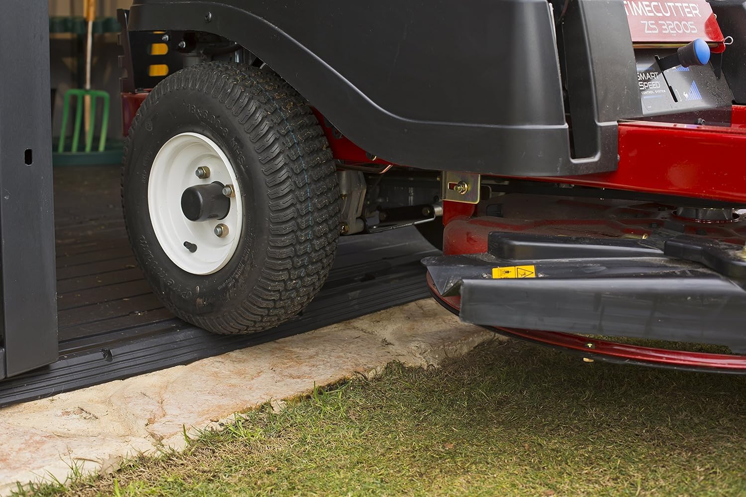 Riding lawn mower wheel at the shed threshold, illustrating the low‑profile floor and ramp access