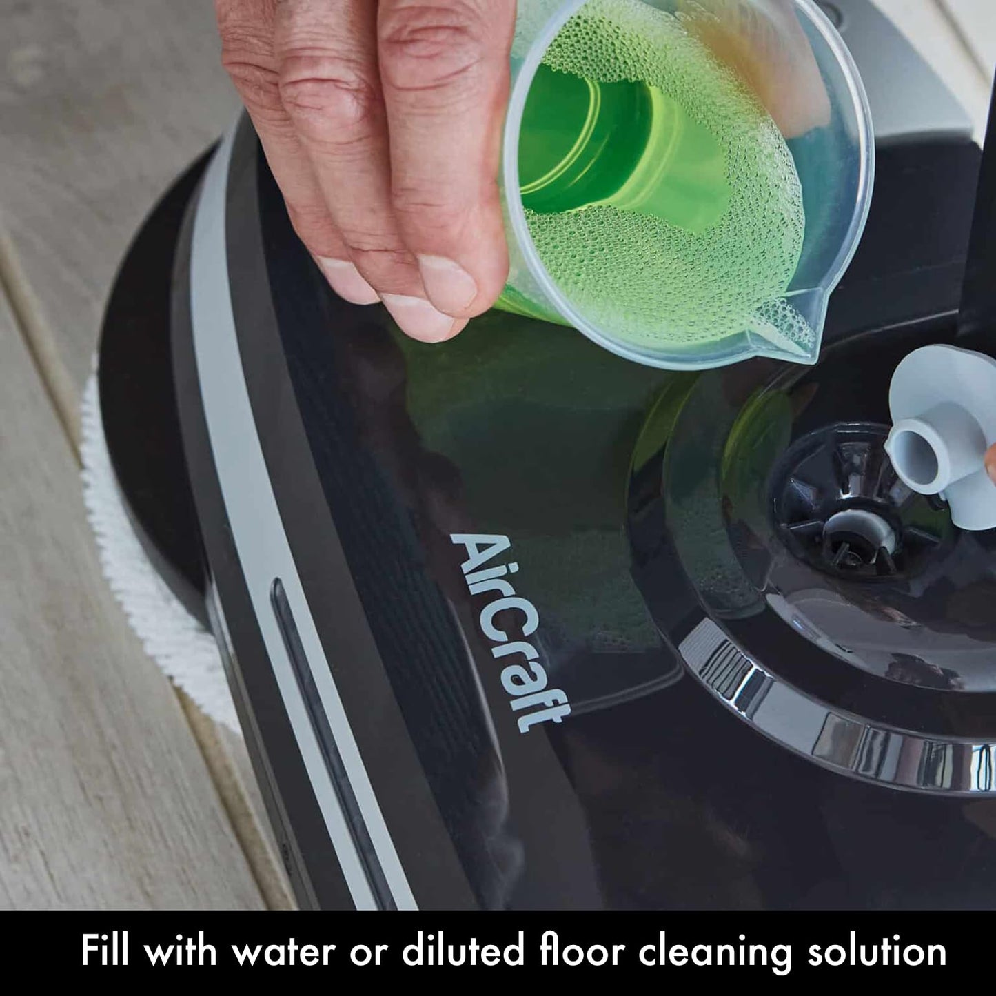 Hand pouring green cleaning solution from a measuring cup into the PowerGlide water tank fill port