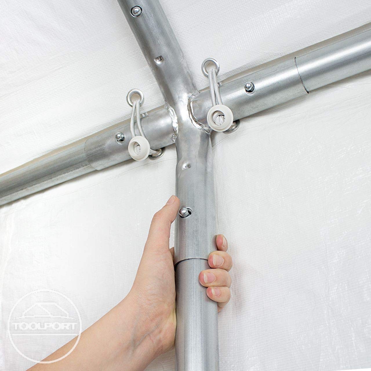 Close-up of hand gripping a galvanized pole at a cross connector with elastic bungee hooks securing the tarpaulin