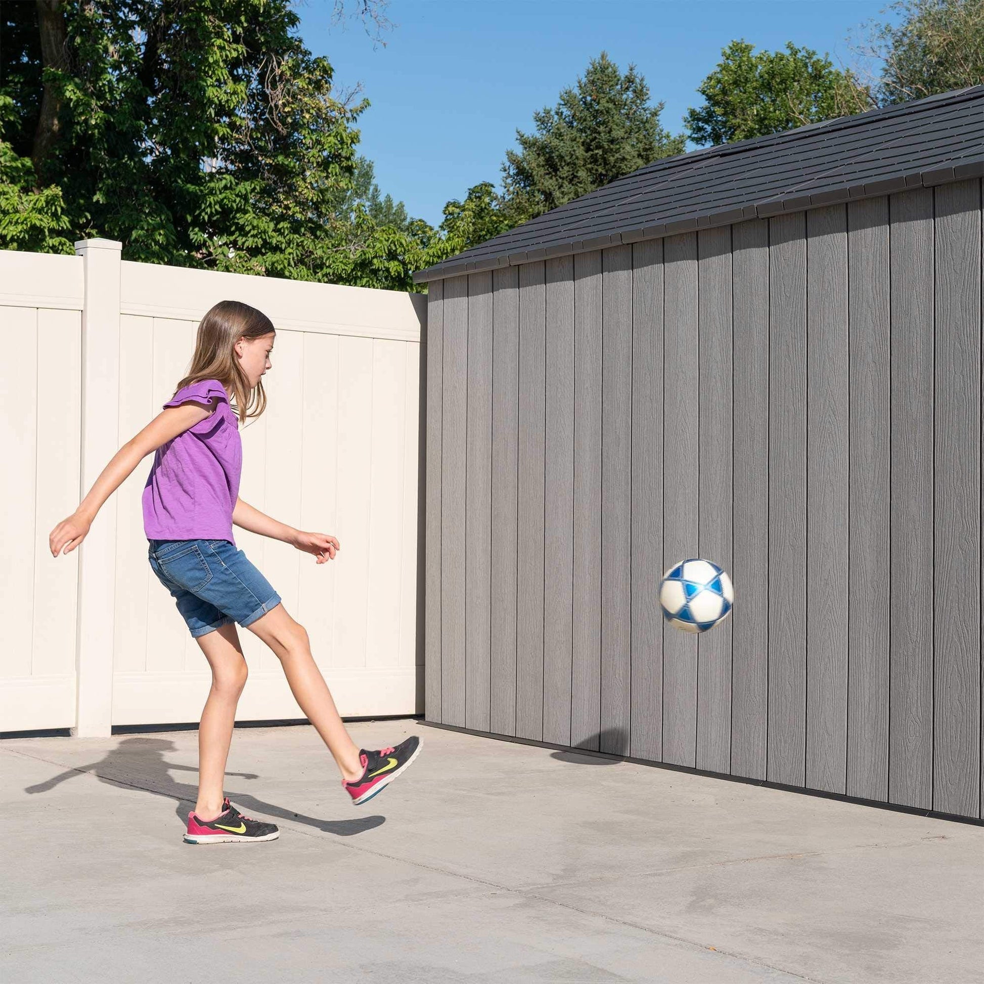 Three-quarter view of the 8×12.5 ft storm dust grey storage shed on a concrete pad next to lawn and flowerbed.