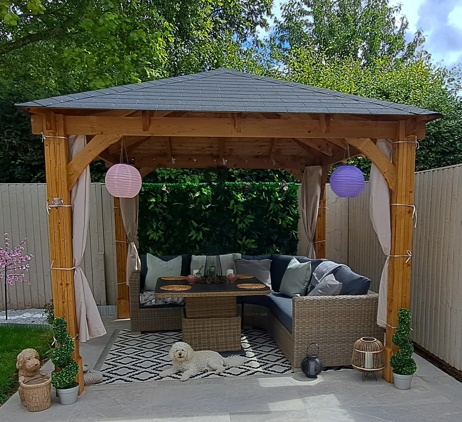 Front view showing the gazebo’s grey shingle roof and supporting timber beams with trees in the background