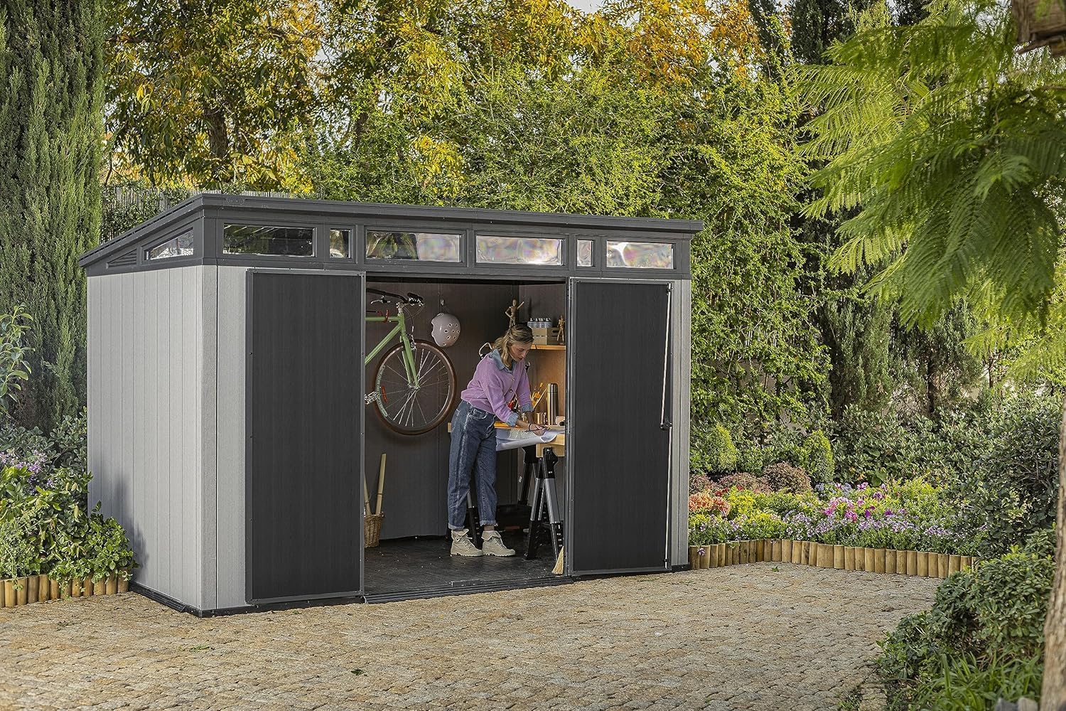 Garden scene with shed doors open; person working at a small bench inside and a bicycle on the wall