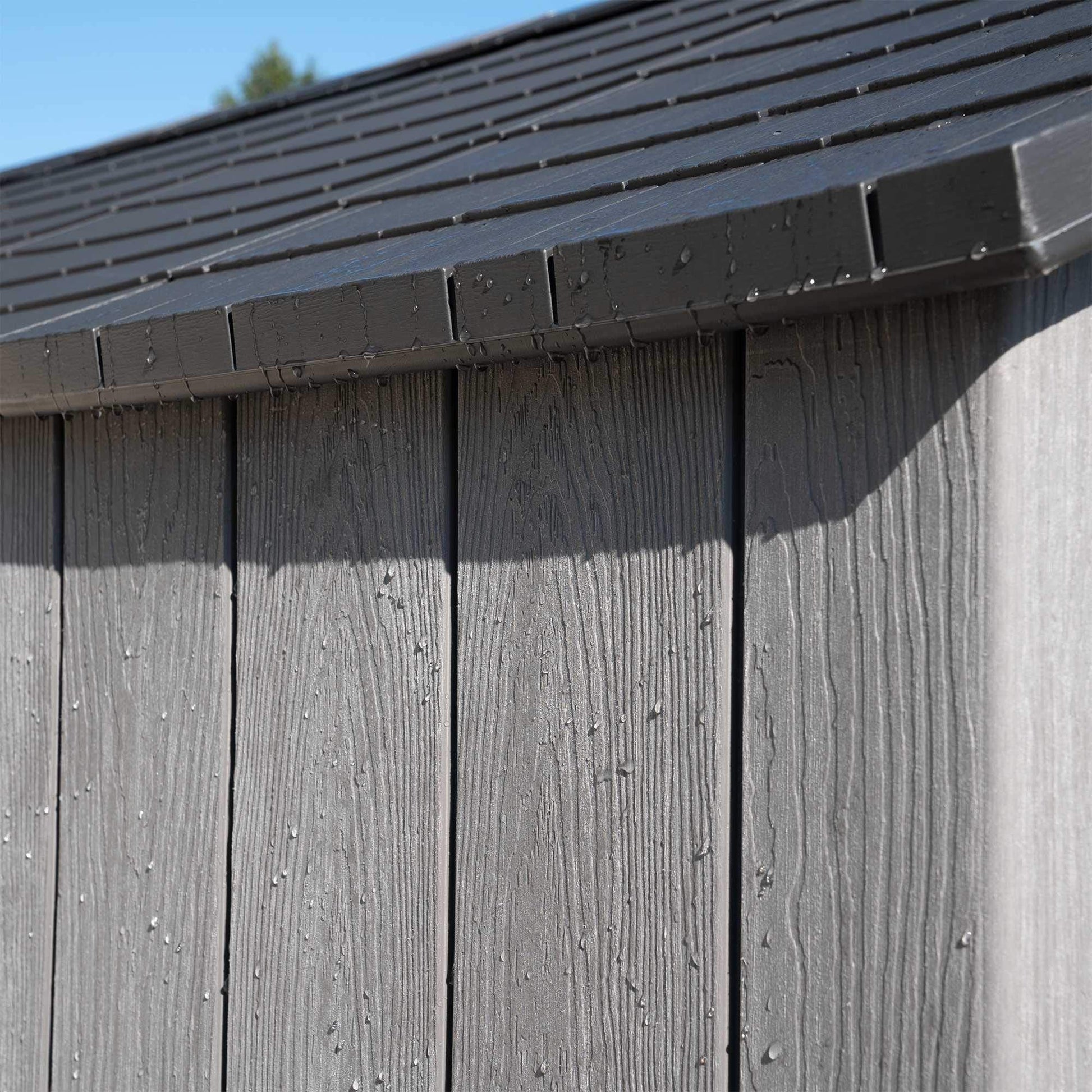 Detail close-up of the dark roof edge and textured wood‑effect wall panels with water droplets.