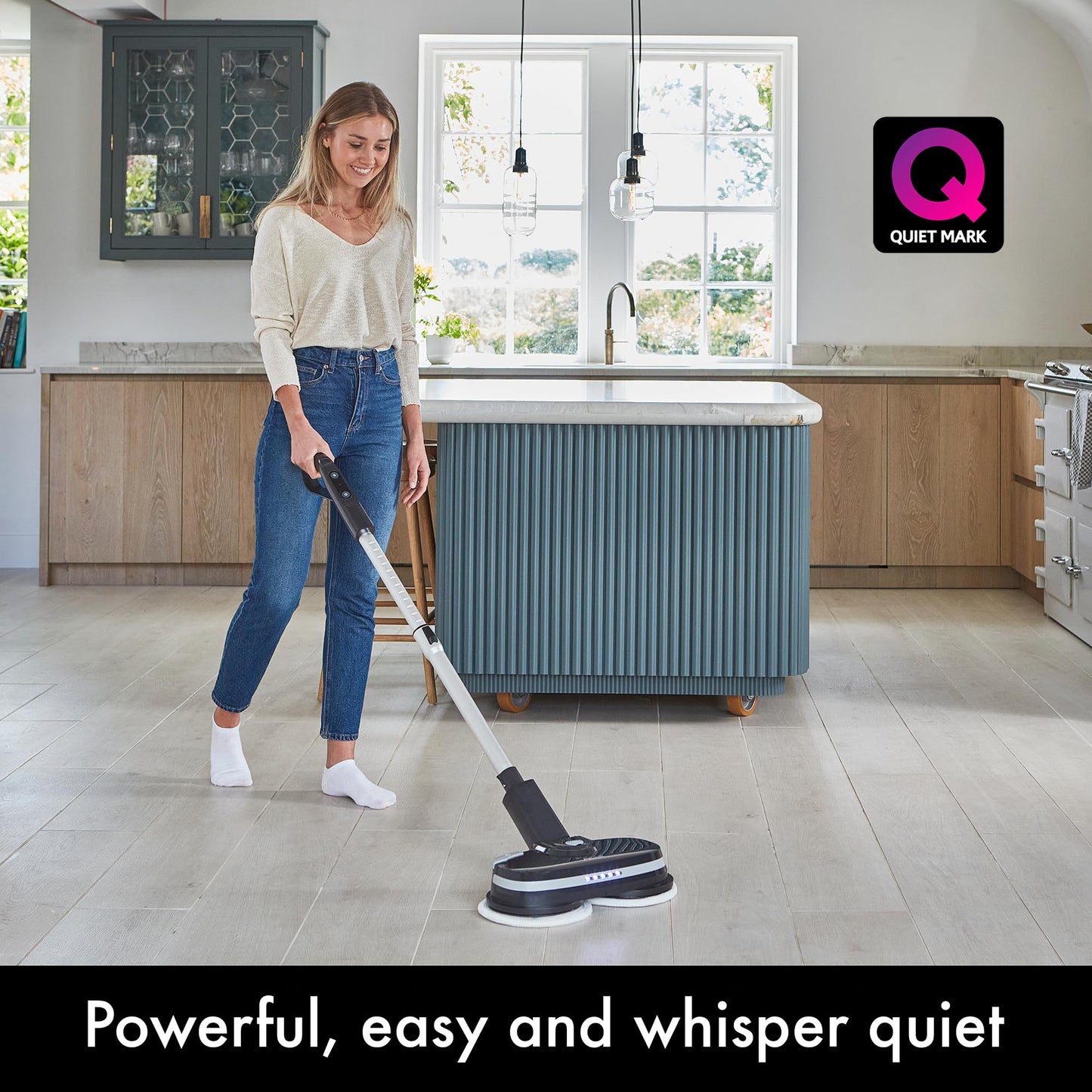 Person cleaning a kitchen floor with the PowerGlide cordless cleaner; Quiet Mark logo visible on wall