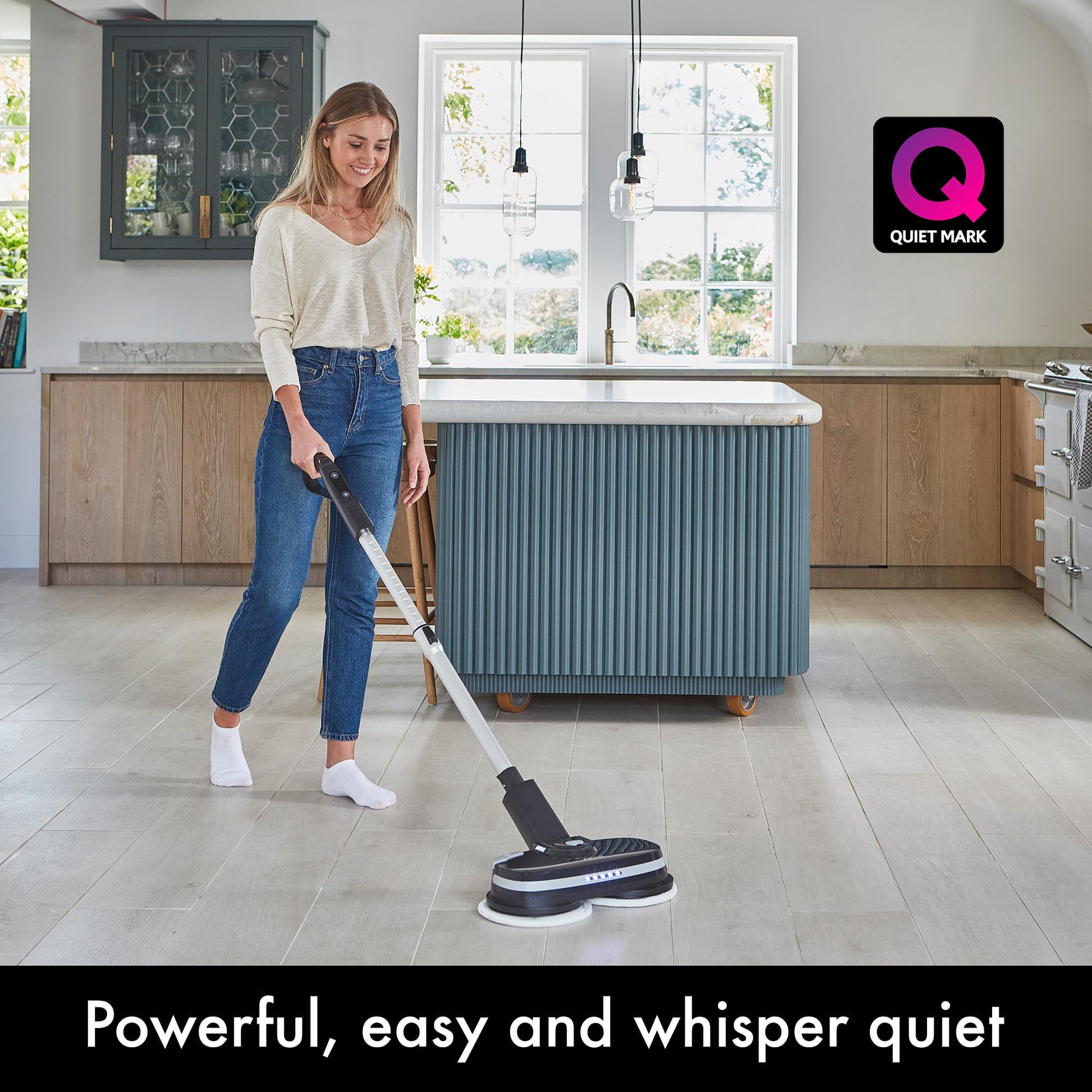 Person cleaning a kitchen floor with the PowerGlide cordless cleaner; Quiet Mark logo visible on wall