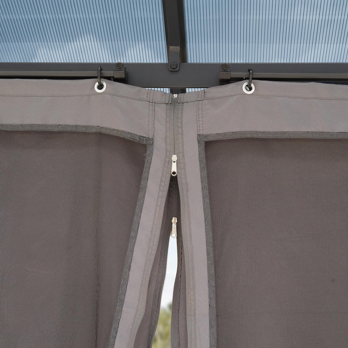 Top of a side curtain with metal grommets on hooks and a central zipper joining two mesh panels.
