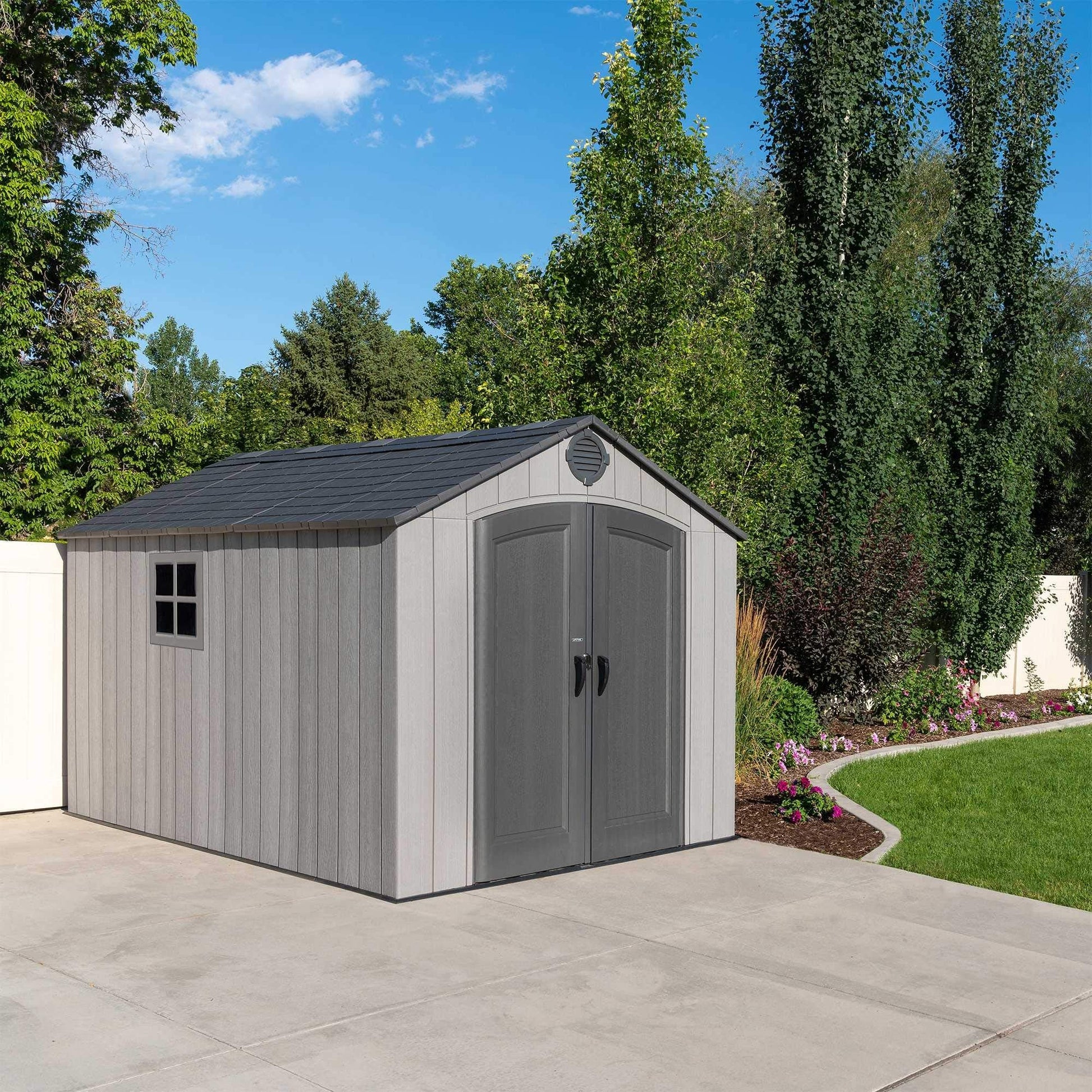 Shed gable and roof with circular vent set against tall backyard trees and a clear blue sky.
